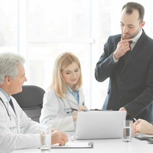 Two seated doctors look at a computer with a man in a suit.