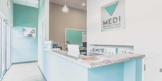 A modern Medi-Weightloss clinic reception area with a sleek front desk, branded signage, and a clean, inviting atmosphere. | Medi-Weightloss